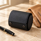 Black 1-slot leather watch roll closed, beside a fountain pen and leather gloves