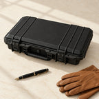 Black protective watch case closed, beside a fountain pen and leather gloves