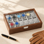 12-slot walnut watch display box closed, beside a fountain pen and leather gloves