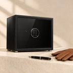 Black leather winder safe closed with its keypad lock, beside a pen and gloves