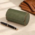 Olive barrel travel case closed, beside a fountain pen and leather gloves