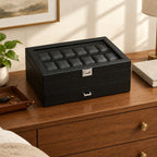 24-slot black faux leather watch box on a wooden chest of drawers