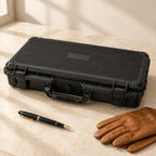 24-slot hard-shell watch case closed, beside a fountain pen and leather gloves