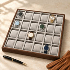 24-slot walnut watch tray beside a fountain pen and leather gloves