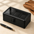 3-slot black aluminum watch box closed, beside a fountain pen and leather gloves