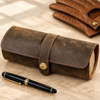 3-slot crazy horse leather watch roll closed, beside a fountain pen and leather gloves