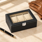 3-slot black faux leather watch box closed, beside a fountain pen and leather gloves