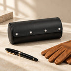 Faux leather watch roll closed, beside a fountain pen and leather gloves