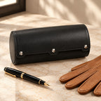 Black faux leather watch roll closed, beside a fountain pen and leather gloves
