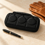 3-slot hard-shell watch case closed, beside a fountain pen and leather gloves