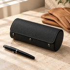 Black 3-slot leather watch roll closed, beside a fountain pen and leather gloves