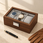 3-slot walnut-finish watch box closed, beside a fountain pen and leather gloves