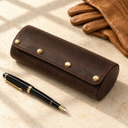 3-watch leather barrel case closed, beside a fountain pen and leather gloves