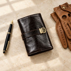 4-slot leather roll-up watch pouch closed, beside a fountain pen and leather gloves