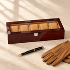 5-slot high-gloss wooden watch box with a glass lid closed, beside a fountain pen and leather gloves