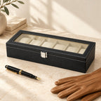6-slot faux leather watch box closed, beside a fountain pen and leather gloves