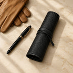 6-slot pebbled leather watch roll closed, beside a fountain pen and leather gloves