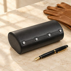 6-watch black roll travel case closed, beside a fountain pen and leather gloves