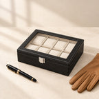 8-slot black faux leather watch box closed, beside a fountain pen and leather gloves