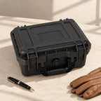Black protective watch case closed, beside a fountain pen and leather gloves