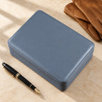 Gray zippered leather watch box closed, beside a fountain pen and leather gloves