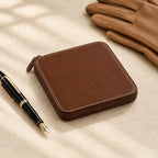 Brown zippered watch case closed, beside a fountain pen and leather gloves