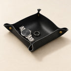 Black valet tray with brass snap corners, holding a watch and a ring
