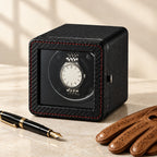 Compact watch winder beside a fountain pen and leather gloves