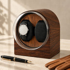 Dark wood-grain watch winder beside a fountain pen and leather gloves