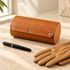 Brown faux leather watch roll closed, beside a fountain pen and leather gloves