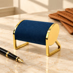 Gold-tone metal watch stand beside a fountain pen and leather gloves