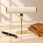 Gold-tone T-bar watch stand beside a fountain pen and leather gloves