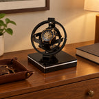 Gyroscope watch winder on a wooden chest of drawers beside a valet tray and a book