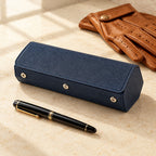 Hexagonal 3-slot watch case in navy with orange interior, beside a fountain pen and leather gloves