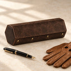 Hexagonal leather watch case closed, beside a fountain pen and leather gloves