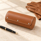 Closed coffee leather watch roll beside a fountain pen and leather gloves