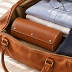 Closed leather watch roll in a weekender bag beside folded shirts