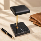 Black marble watch stand beside a fountain pen and leather gloves