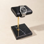 Black marble watch stand with a gold stem and black leather pillow holding a watch