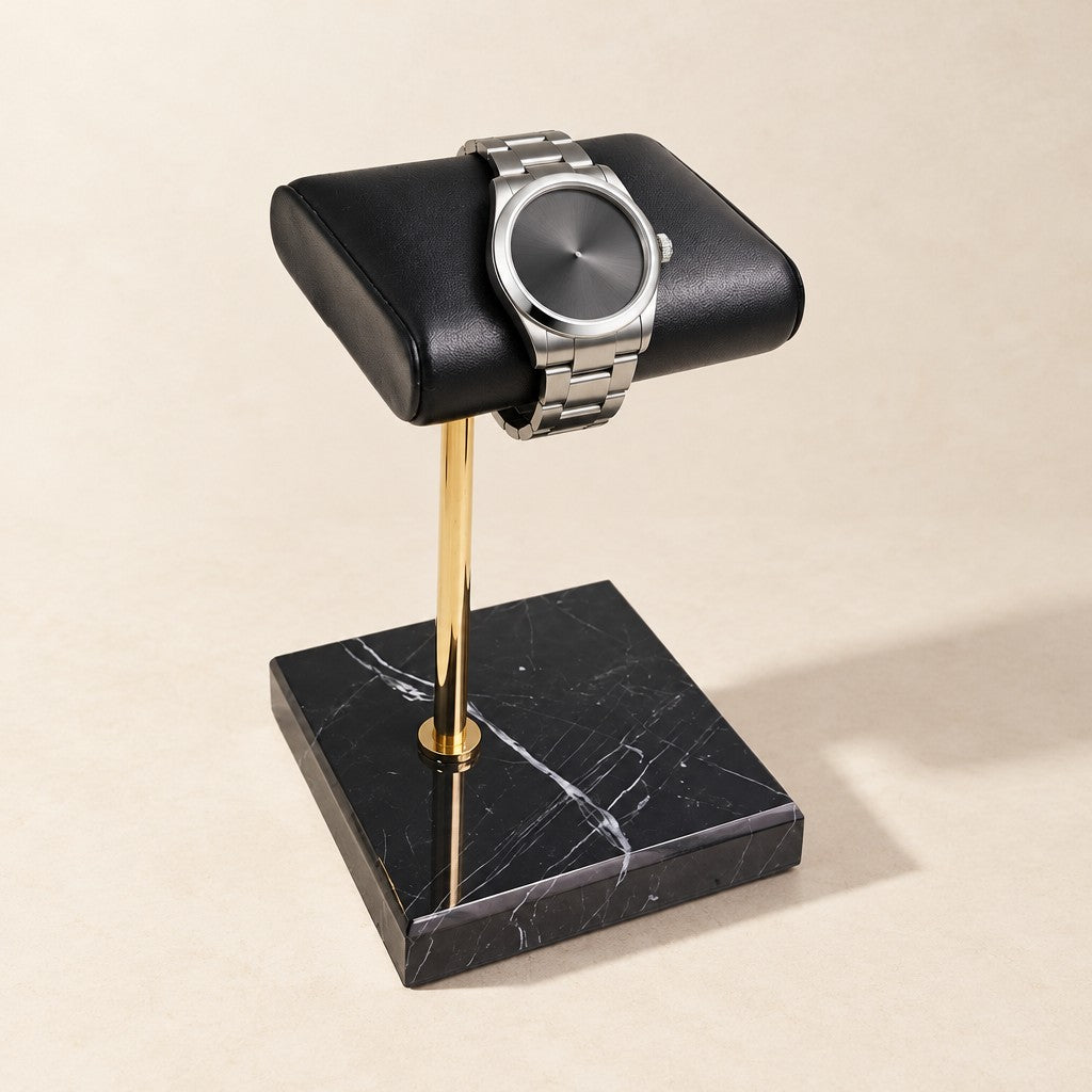 Black marble watch stand with a gold stem and black leather pillow holding a watch