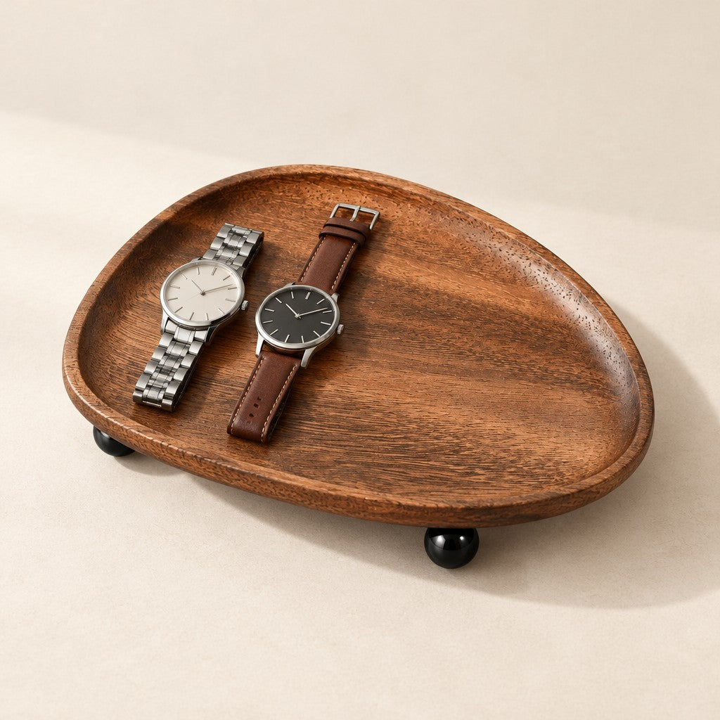 Pebble-shaped solid wood catchall tray on black ball feet, holding two watches