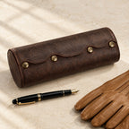 Oval leather watch roll closed, beside a fountain pen and leather gloves