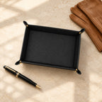 Pebbled leather valet tray beside a fountain pen and leather gloves