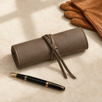 Khaki leather watch roll rolled and tied, beside a fountain pen and leather gloves