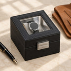 Black single watch box with glass window closed, beside a fountain pen and leather gloves