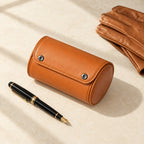 Tan single watch roll closed, beside a fountain pen and leather gloves