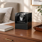 Single watch winder on a wooden dresser beside a book and a leather tray