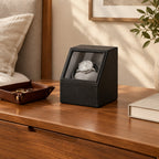 Single watch winder on a wooden dresser beside a valet tray and a book