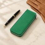 Zippered single watch case closed, beside a fountain pen and leather gloves