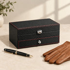 Two-tier carbon-pattern watch box with a jewelry drawer closed, beside a fountain pen and leather gloves